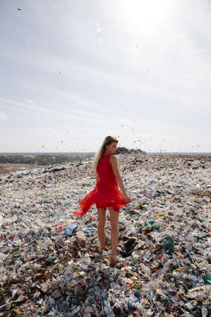 Nature pollution activist at a huge trash dump outdoors - Young blonde woman in a red dress - Looking at all the human waste and plastic in our world - Seagulls flying in Eastern Europe Latvia Rigaの写真素材