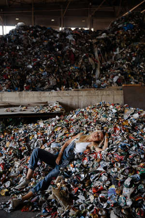 Laying down - Nature pollution activist at a huge trash dump - Young blonde woman - Looking at all...