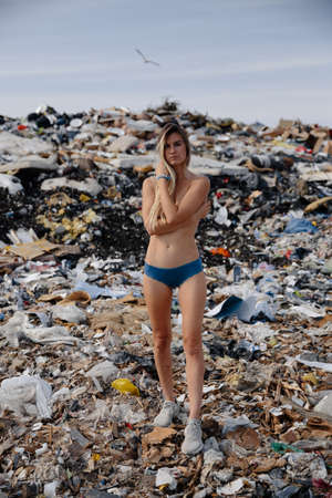 Nature pollution activist at a huge trash dump outdoors - Naked topless blonde woman - Looking at...
