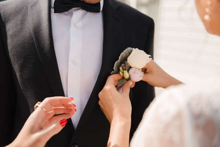 Wedding boutonniere being pinned to a groom suit by bride hand close up in Eastern European Baltic Riga Latviaの写真素材