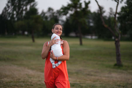 Young mother holding and playing with her baby boy child in city park standing wearing bright red dress - Son wears white cap - Family values warm color summer scene handheldの写真素材