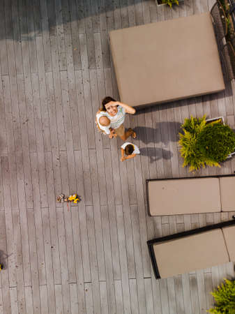 Aerial drone: Young mother playing and having fun with her baby boy son brothers in a green garden with cars - Family values warm color summer scene - Eastern European Latvia Rigaの写真素材