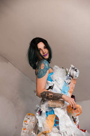 Portrait of smiling female eco fighter wearing trash dress made of plastic and cardboard helping...
