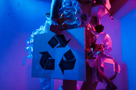 RECYCLE SIGN: Portrait of smiling female eco fighter wearing trash dress made of plastic and...