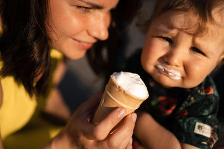 Mother feeding baby child boy ice-cream - Young mom and her baby eat white vanilla creamy dessert - Sits in a baby carriage pram - Caucasian family 1 year oldの写真素材