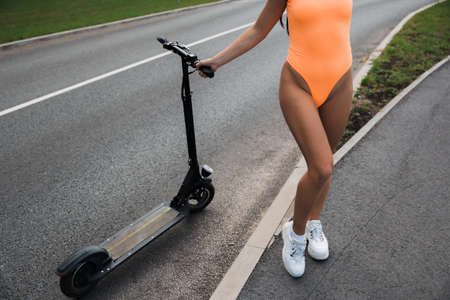 Sexy hot woman riding electric scooter at parking lot wearing body swimwear lingerie and sunglasses - Emission free eco friendly transportationの写真素材