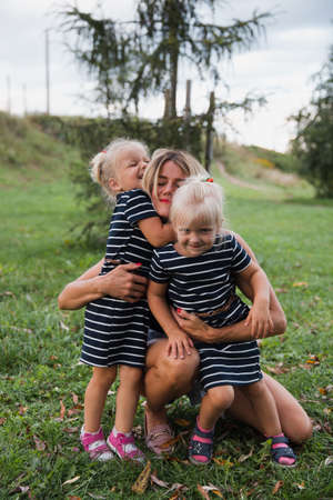 Twin blonde little girls sitting on electric scooter in park with their motherの写真素材