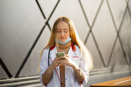 Female nurse uses smartphone during break outdoors