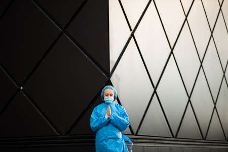 Epic shot of female doctor or nurse praying in medical mask and surgical cap