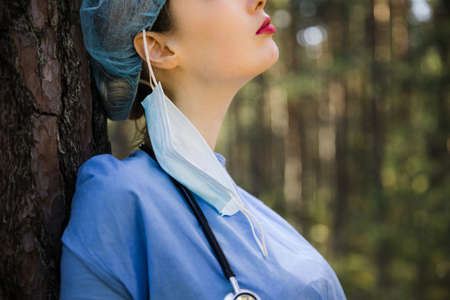 Tired but happy female doctor took off surgical mask in forest. Wear surgical mask and gownの写真素材