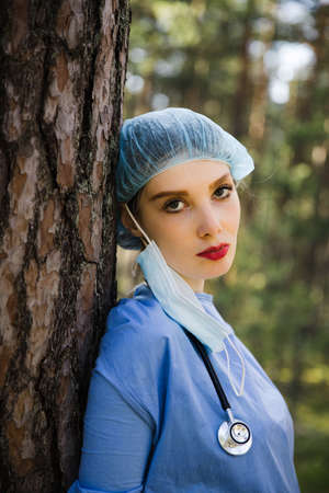 Tired female doctor stands at tree and looks at youの写真素材