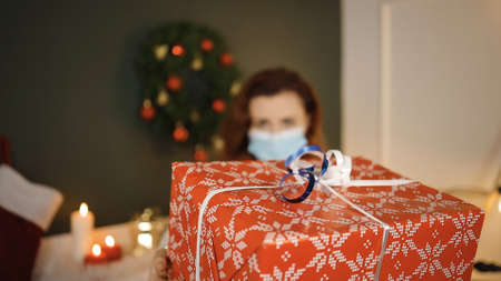 Huge red gift box in hands of young woman in medical mask