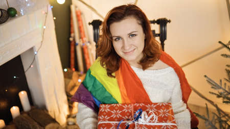 Smiling young woman in LGBT rainbow flag holds large red gift box
