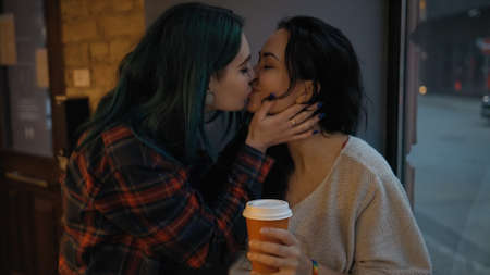 Lesbian young woman comes and hugs her partner with coffee cup in handsの写真素材