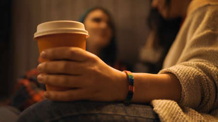 Close view: Cup of coffee in hand of lesbian woman chatting with girlfriend in cafeの写真素材