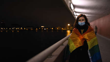 Exhausted lesbian woman in medical mask and large rainbow flagの写真素材