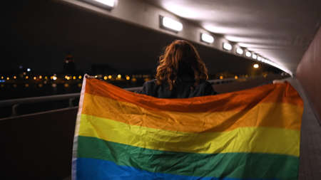 Backside view: LGBT woman walking with large rainbow flagの写真素材
