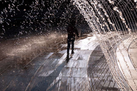Happy attractive boy running. Water splash in fountain in sunny day.の写真素材