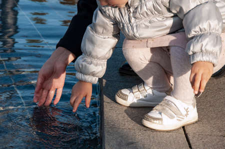 mother and daughter sit on the edge of the pond and dip their hands in water