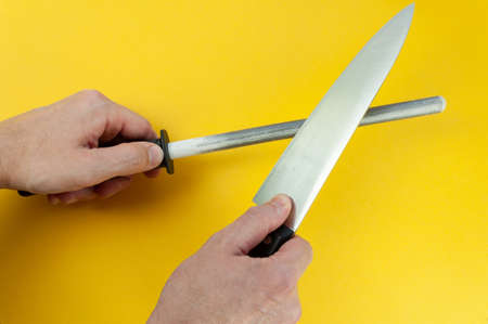 Man hand sharpenes knife on yellow background. Knife sharpening using a knife grinder.