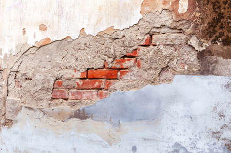 Grungy retro red brick walls with broken gray white stucco. View of the eroded and damaged cracked plaster fence. Vintage wall structure with peeling plasterの写真素材