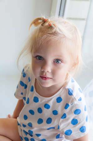 Close up portrait of adorable baby girl sitting on the windowsillの写真素材