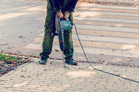 Worker with pneumatic hammer drill equipment. Road repairing works with jackhammer