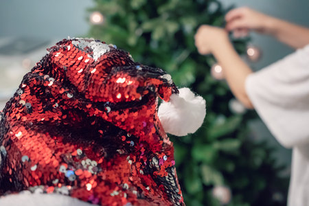 Women's hands decorate the Christmas tree with balls and toys. Red Santa Claus Hat on Christmas tree. New Year mood. Party and holiday celebration conceptの写真素材