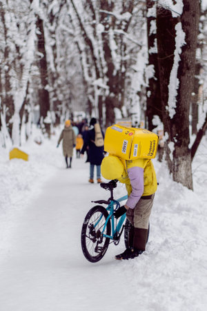 Krasnodar, Russia - January 24 2022: Courier, a food delivery man with a thermal bag on his back repairing a bicycleのeditorial素材