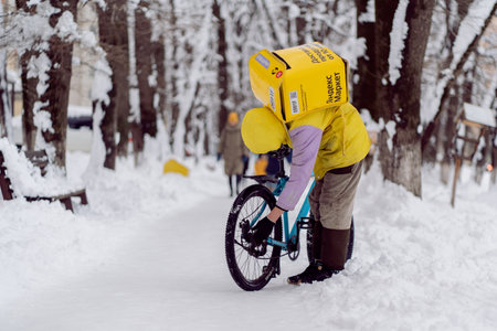 Krasnodar, Russia - January 24 2022: Courier, a food delivery man with a thermal bag on his back repairing a bicycleのeditorial素材