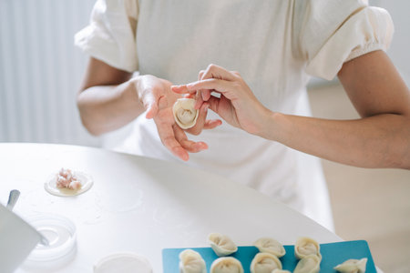 Woman making dumplings. Front view of womans hands making meat dumpling. Cook hands lay out minced meat on dumplingsの写真素材
