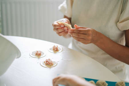 Woman making dumplings. Front view of womans hands making meat dumpling. Cook hands lay out minced meat on dumplingsの写真素材