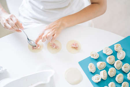 Woman making dumplings. Front view of womans hands making meat dumpling. Cook hands lay out minced meat on dumplingsの写真素材