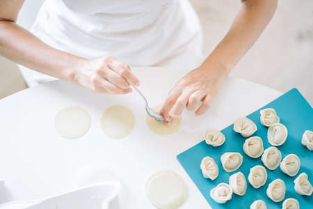 Woman making dumplings. Front view of womans hands making meat dumpling. Cook hands lay out minced meat on dumplingsの写真素材