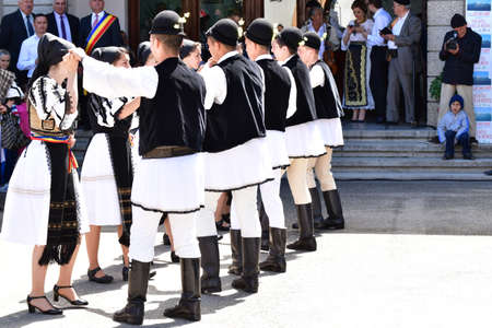 Romanian folk dancers in national linen pastoral costumes, sewn with traditional black motifs, men...