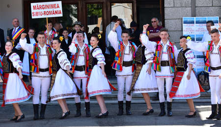 Folk dancers from Transylvania wear astrakhan lambskin hats adorned with peacock beads and feathers, white linen shirts and pants, wide leather belt, tricolor diagonal representing the national flagのeditorial素材