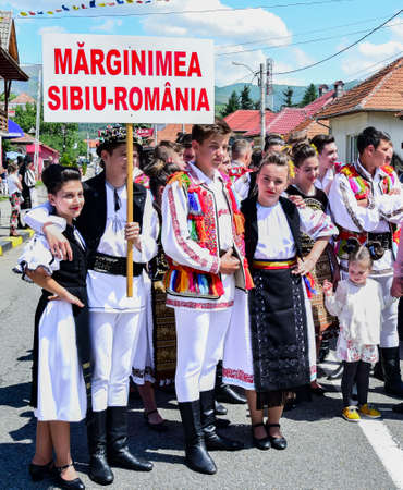 Folk dancers from Transylvania wear astrakhan lambskin hats adorned with peacock beads and feathers, white linen shirts and pants, wide leather belt, tricolor diagonal representing the national flagのeditorial素材