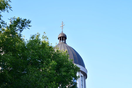 The dome of the church against the blue sky and green trees.