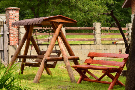 Wooden swing in the backyard of a country house with a fence and treesの写真素材