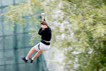 A person is suspended in the air, holding onto a rope. The person is dressed in a black sweater and white shorts.の写真素材