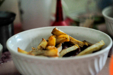 Fried potato chips in a white bowl on the kitchen table.