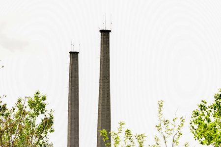 Industrial chimney with white sky and green trees in the backgroundの写真素材