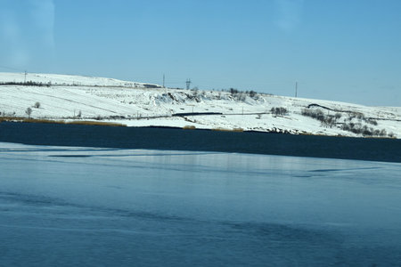 Winter landscape with snow-covered fields and river under the blue sky
