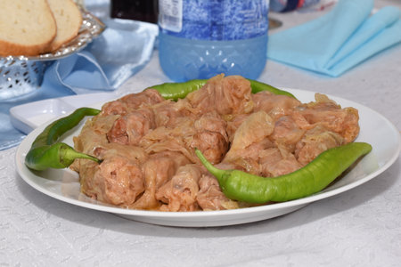 Cabbage rolls on a white plate with green peppers and bread.