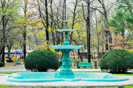 Fountain in the city park on a background of green trees.の写真素材