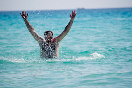 Young man splashing water in the sea on a sunny day.の写真素材