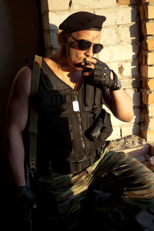 Armed muscular mercenary with cigar on the brick wall backgroundの写真素材