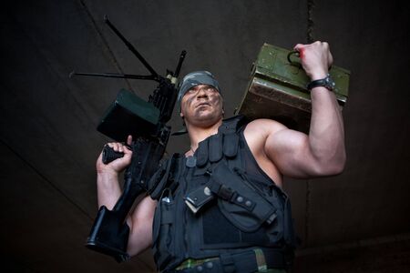 Armed mercenary with submachine gun and box of grenade on the brick wall backgroundの写真素材