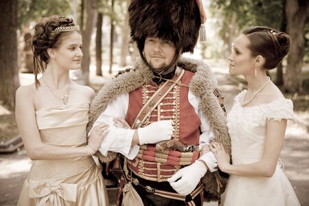 Russian hussar in vintage outfit with two pretty women.の写真素材