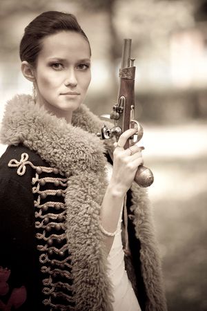 Portrait of pretty woman with pistol dressed in vintage dress and accessories. 